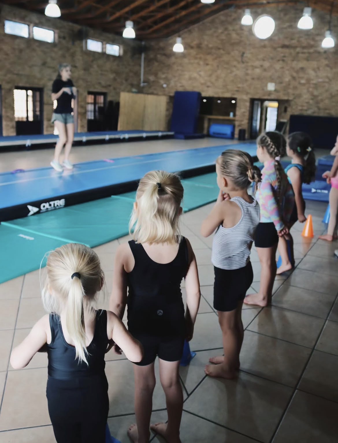 Young gymnasts lined up watching a coach demonstrate on the tumbling track