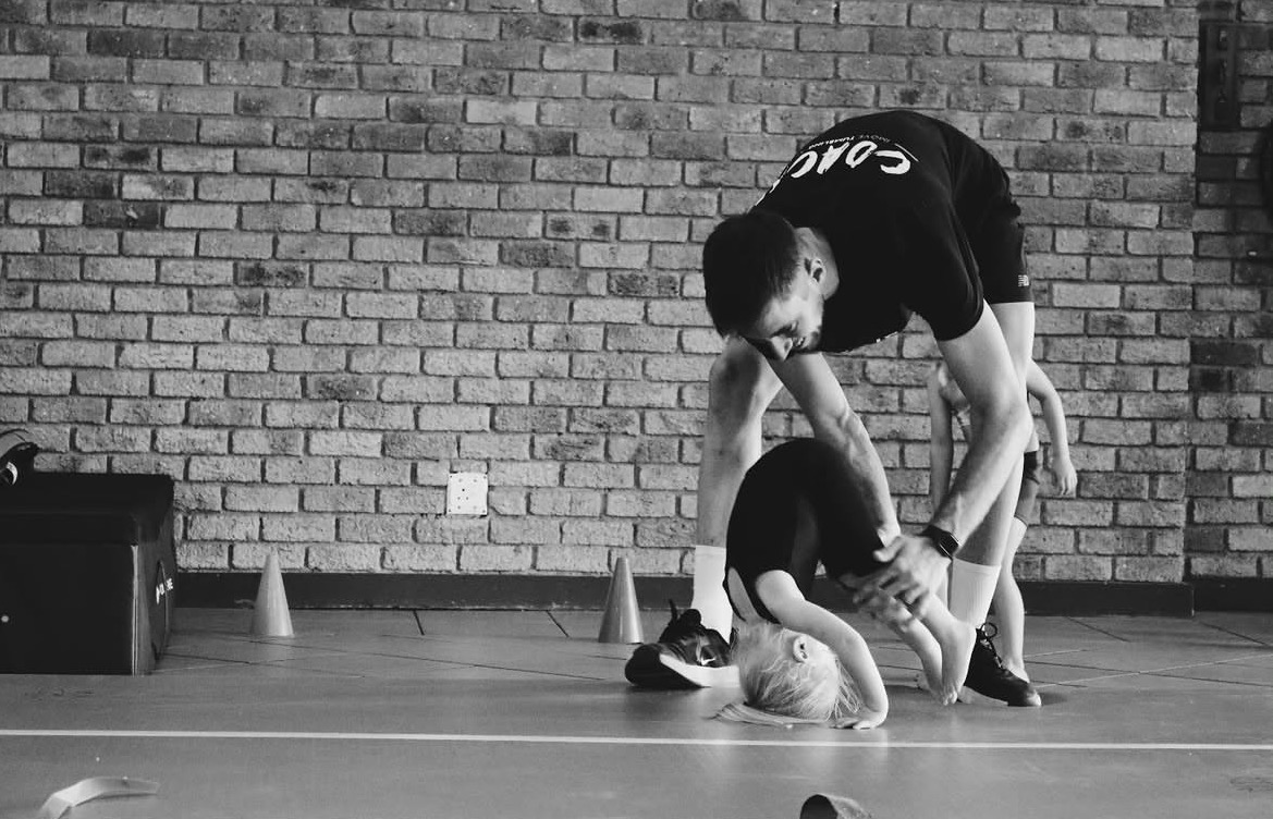 Coach guiding a young gymnast through a backbend drill